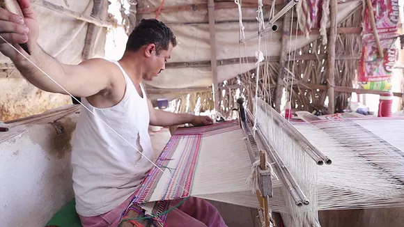 The yarn is put on the warp (tano) on the loom. Weaving is done on a pit loom, where the weaver’s feet are below the loom while he sits at the ground level, giving it the name of pit loom.  Pic: Shamji Valji  30 stades